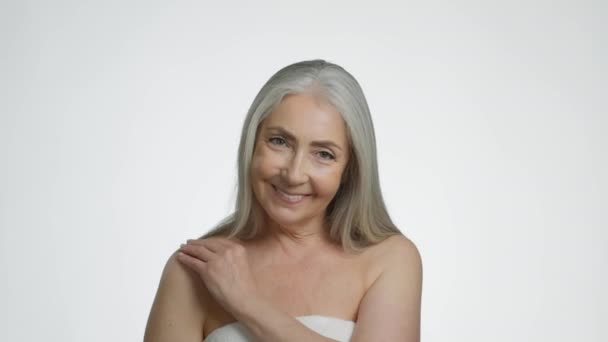 Прекрасне старіння. Щаслива сіро-волохата жінка модель позує з голими плечима, торкається її шкіри і грає з волоссям, посміхається на білому фоні студії, повільний рух
 - Кадри, відео