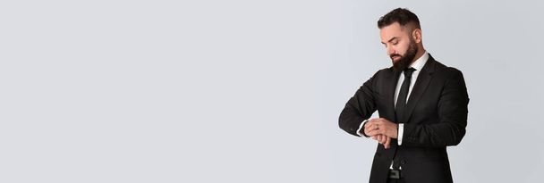 Time Management. Handsome Young Businessman In Black Suit Looking At Wristwatch, Wide Horizontal Banner With Confident Male Entrepreneur Posing Isolated On Light Grey Background, Copy Space - Foto, afbeelding