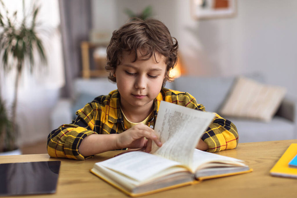 Εγχώρια διαδικασία μάθησης. Χαριτωμένο μικρό αγόρι μελέτη για να διαβάσετε, διαβάζοντας το βιβλίο στο γραφείο, μελέτη στο σπίτι, ελεύθερος χώρος - Φωτογραφία, εικόνα
