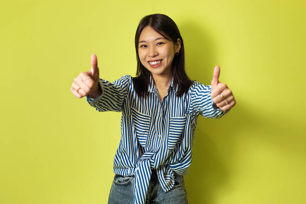 I Like It. Cheerful Female Gesturing Thumbs Up With Both Hands Smiling Looking At Camera Posing Standing Over Yellow Studio Background. Lady Approving Offer Concept - Foto, afbeelding