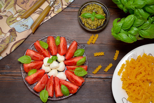ingredients for cooking dinner, raw pasta, appetizer antipasto caprese, pesto sauce on the kitchen table - Photo, image