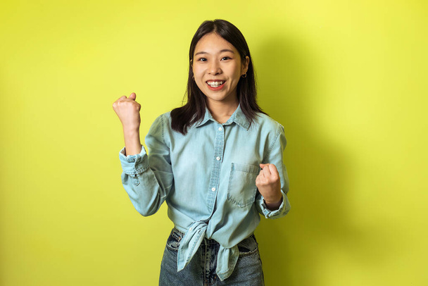 Cheerful Korean Female Gesturing Yes With Both Hands Celebrating Success Standing Over Yellow Studio Background. Happy Woman Shaking Fists. Joy Of Victory Concept - Fotó, kép