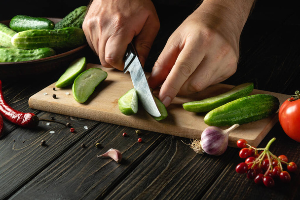Slicing cucumbers on a cutting board by the hands of a cook for preparing a vegetable salad. Menu for a restaurant or hotel. - Zdjęcie, obraz