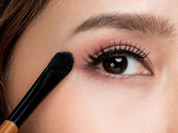 Closeup ardent young woman with healthy fair skin applying her eyeshadow with brush. Female model with fashion makeup. Beauty and makeup concept. - 写真・画像