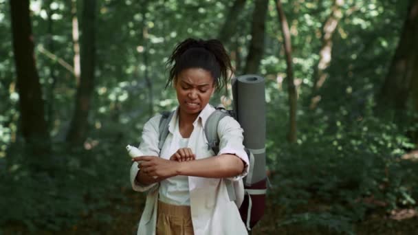 Annoying insects. Young irritated african american woman tourist scratching her hand after mosquito bite, holding repellent spray, standing in forest, slow motion, free space - Filmati, video