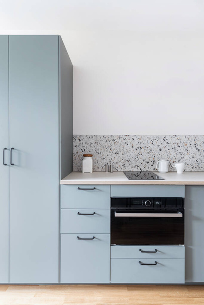современный дизайн интерьера на кухне с серым деревянным шкафом, белой столешницей и современной техникой или электрической печью и индукционной стеклянной керамической плитой - Фото, изображение