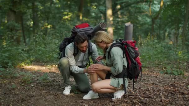 Health problem in journey. Upset woman tourist having trouble feeling knee pain during travel in forest, her loving husband helping her, massaging leg, slow motion - Filmmaterial, Video