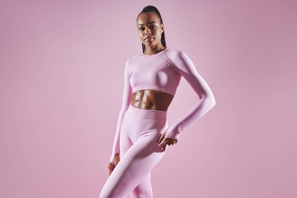 Attractive young African woman in sports clothing standing against pink background - Photo, Image
