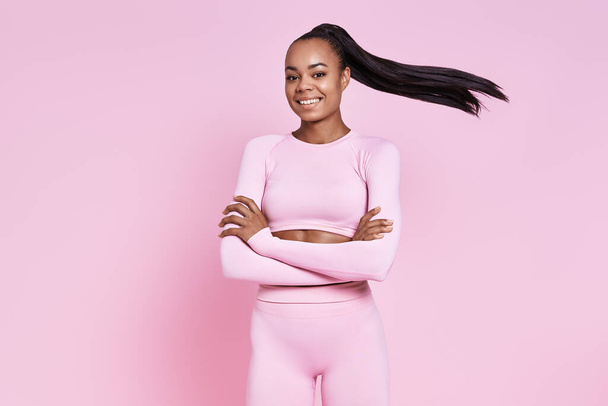Happy young African woman in sports clothing standing against pink background - Zdjęcie, obraz