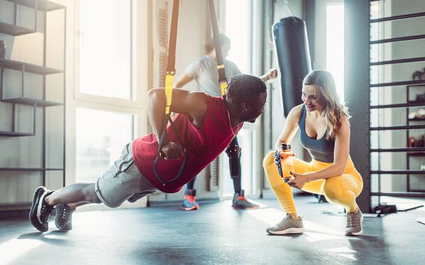 Woman and man at sling trainer in gym during workout - Foto, afbeelding