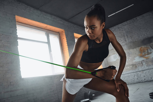 Beautiful young African woman exercising with elastic resistance band in gym - Foto, Imagem