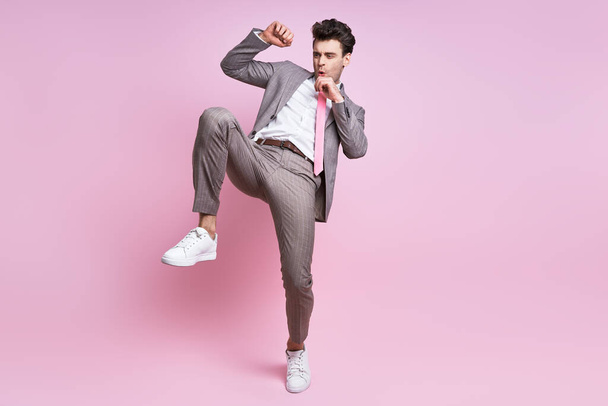 Furious young man in full suit fighting while standing against pink background - Foto, immagini
