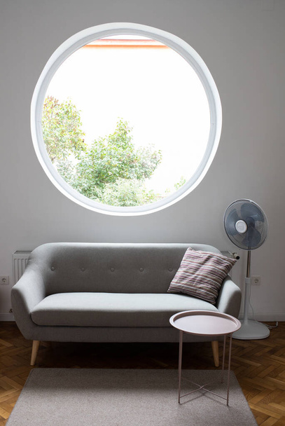 сірий диван у затишній вітальні з круглим вікном
 - Фото, зображення