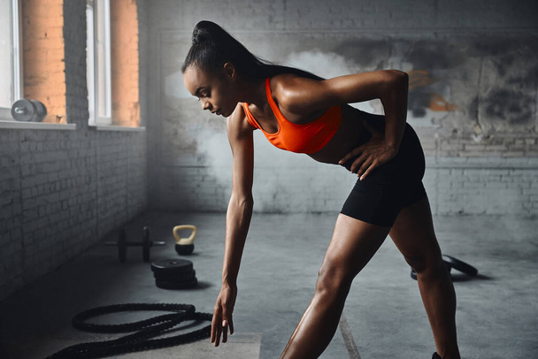 Beautiful young African woman in sports clothing exercising in gym - Foto, imagen