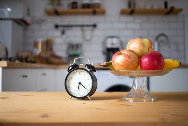 vintage alarm clock and fresh fruit on kitchen table intermittent fasting - Foto, afbeelding