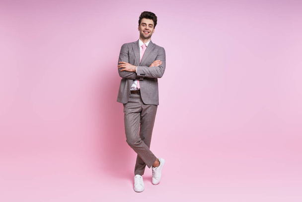 Handsome young man in full suit smiling while standing against pink background - Фото, изображение