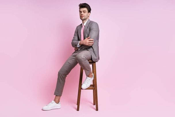 Confident man in full suit sitting on the chair against pink background - Fotografie, Obrázek