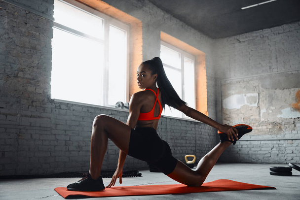 Beautiful young African woman doing stretching exercises in gym - Photo, image