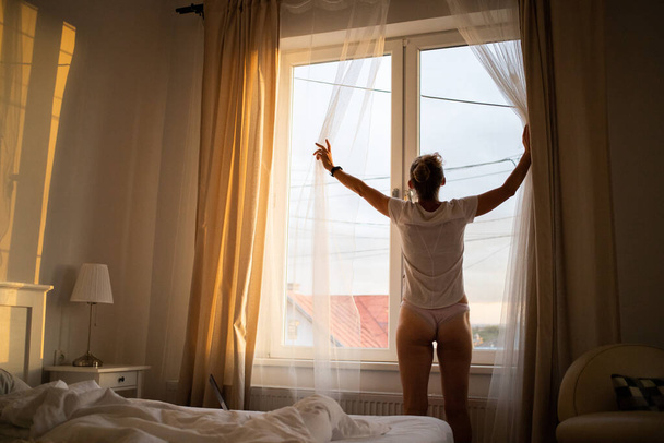 жінка відкриває штори спальні в яскравому сході сонця
 - Фото, зображення