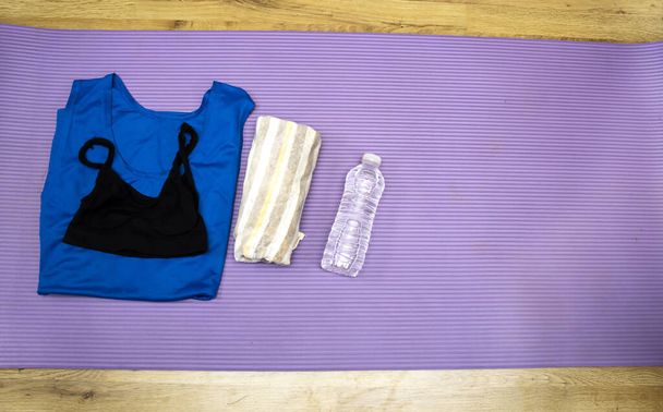 Healthy lifestyle, sport or athlete's equipment set : bottle of water with earphones and sneakers, towel and shirt, phone on purple mat with copy space - Photo, image
