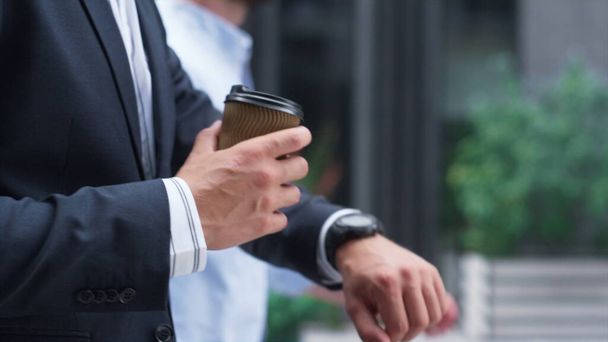 Confident businessman walking hold coffee downtown. Male hand with cup closeup. Unrecognized man finance assistant check time looking at watch on street. Manager go to important client meeting in suit - Photo, Image