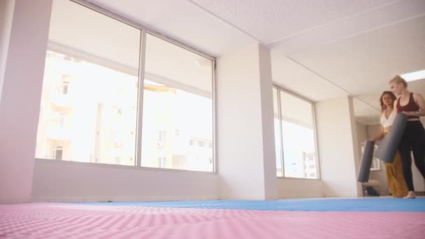 Three women walks in the studio and brings yoga mats with them. Mid shot - Video, Çekim