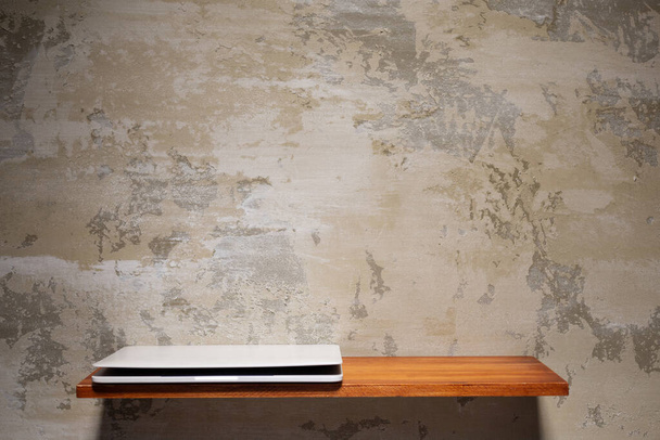 Computer laptop at wooden shelf on wall. Laptop and construction concept on concrete background - 写真・画像