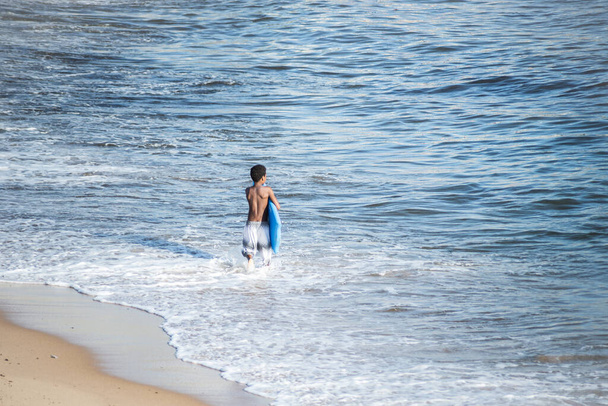 Salvador, Bahia, Brazil - November 01, 2021: Surfer entering the water of Rio Vermelho beach in Salvador, Bahia. - Photo, image