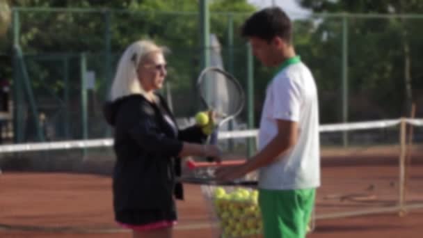 A woman gives a young man a tennis racket and a ball. Mid shot - Video