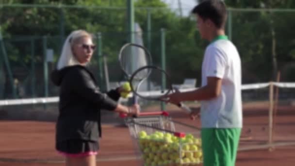 A woman and a young guy communicate on a tennis court. Mid shot - Video