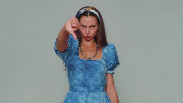 Upset lovely pretty young woman showing thumbs down sign gesture, expressing discontent, disapproval, dissatisfied, dislike. Adult stylish female girl isolated alone on gray studio background indoors - Filmagem, Vídeo