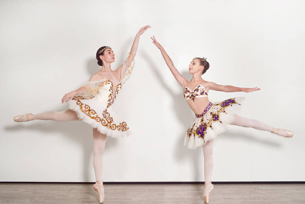 Дві молоді балерини практикують позу балету на білому тлі
 - Фото, зображення