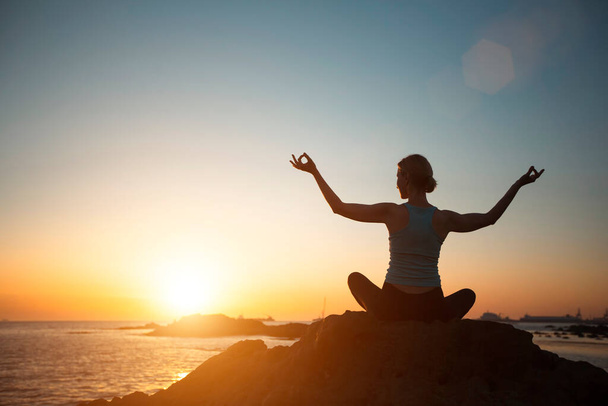 Жінка спортивного будівництва робить йогу, роздумуючи над океанським пляжем під час прекрасного заходу сонця
.   - Фото, зображення