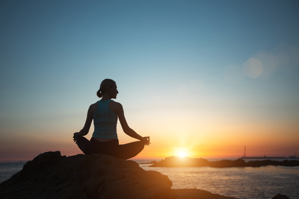 A woman does yoga, meditating on an ocean beach during a beautiful sunset.   - Zdjęcie, obraz