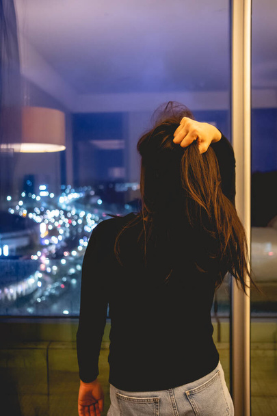 Сексуальная молодая азиатская деловая девушка, держащая волосы перед большим окном с красочными ночными огнями города - Фото, изображение