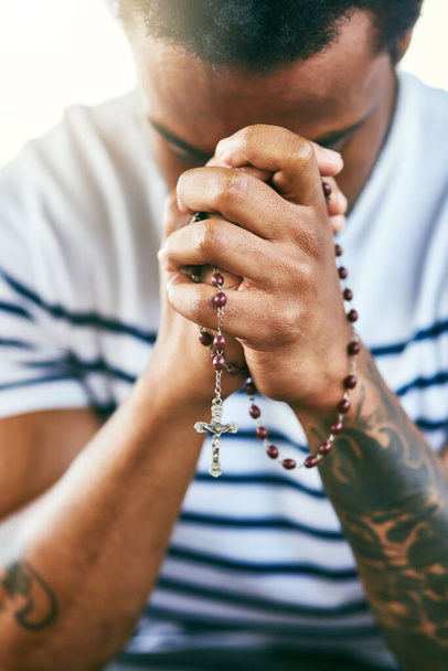 He hears all your prayers. a young man holding his rosary while praying - Zdjęcie, obraz