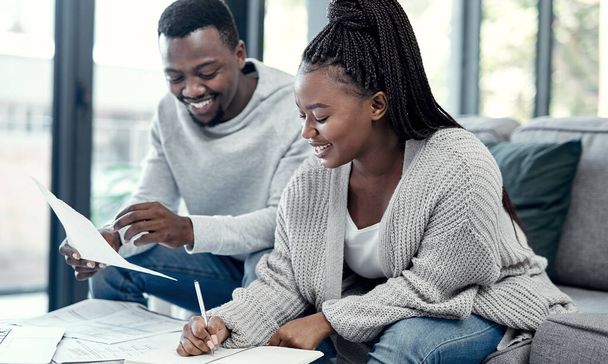 Счастливая афроамериканская пара занимается финансовым планированием, пишет бюджетные документы на диване дома. Улыбающиеся бойфренд и девушка обсуждают страховые счета, сбережения и инвестиции на будущее - Фото, изображение