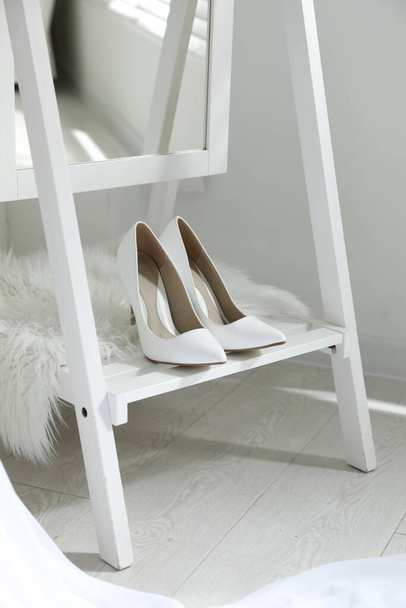 Pair of white wedding high heel shoes on wooden rack indoors - Foto, Imagen