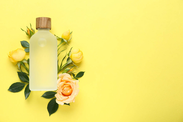 Bottle of rose essential oil and beautiful flowers on pale yellow background, top view. Space for text - Photo, Image