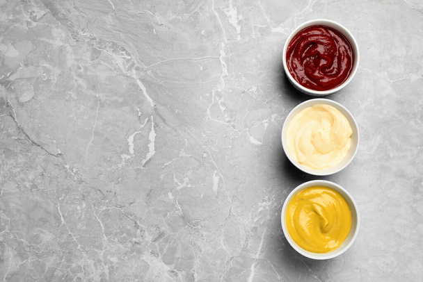 Bowls with mustard, ketchup and mayonnaise on light grey table, flat lay. Space for text - Foto, imagen