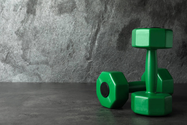 Green vinyl dumbbells on table against grey background. Space for text - Foto, Imagen