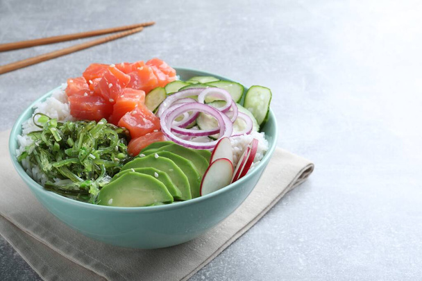 Delicious poke bowl with salmon, seaweed and vegetables served on light grey table. Space for text - Foto, afbeelding