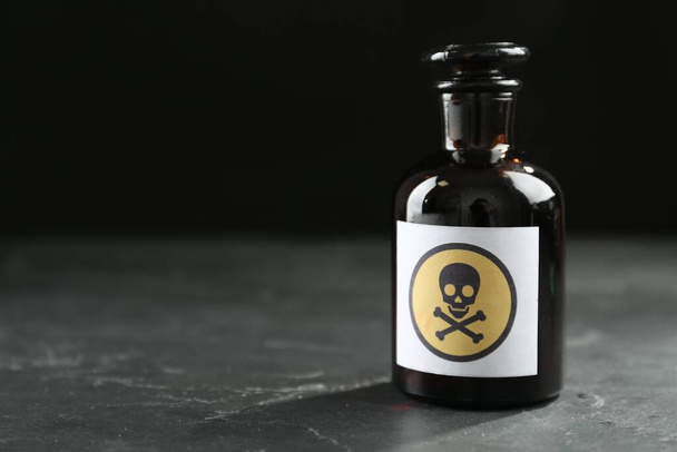 Glass bottle of poison with warning sign on black table. Space for text - Photo, image