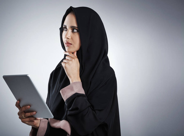 Thinking it over. an attractive young businesswoman using her tablet while standing against a grey background - Foto, immagini