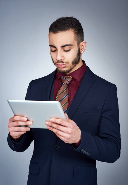 Technology can be a helpful tool in business. Studio shot of a handsome young businessman using a tablet against a grey background - Foto, Imagen