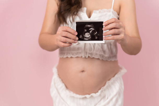 close up pregnant woman showing ultrasound photo of baby on pink background  - Fotó, kép