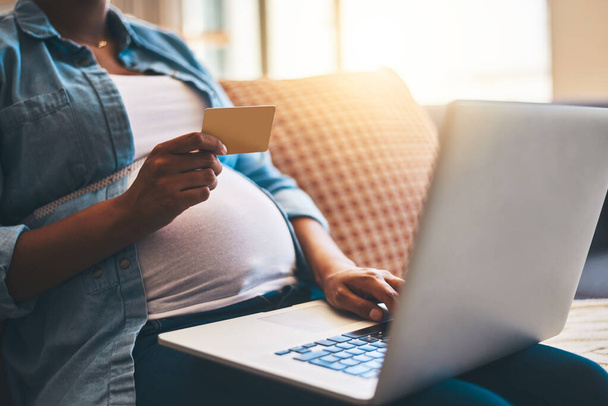 Not every gift is gotten at a baby shower. a pregnant woman using a laptop and credit card on the sofa at home - Photo, Image