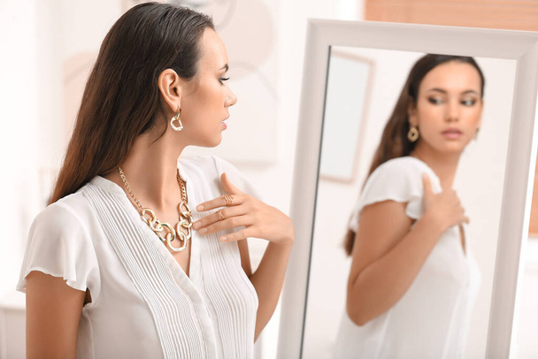 Beautiful young woman with stylish jewelry looking in mirror at home - Zdjęcie, obraz