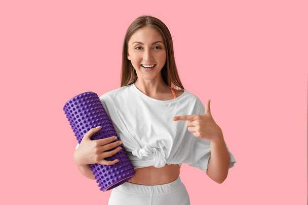 Young woman pointing at foam roller on pink background - Foto, afbeelding