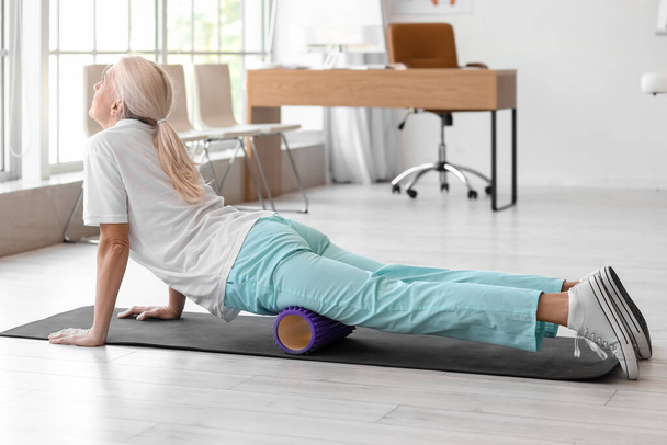 Mature physiotherapist training with foam roller in rehabilitation center - Photo, image